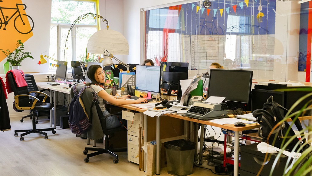 Пространство open space. За рабочим местом сидит девушка-сотрудник. На стене нарисован велосипед.